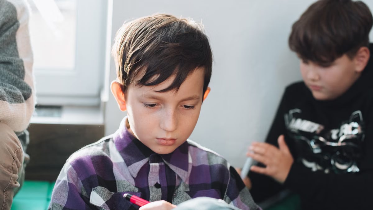 A young schoolboy concentrating while writing with a pen in a classroom setting.